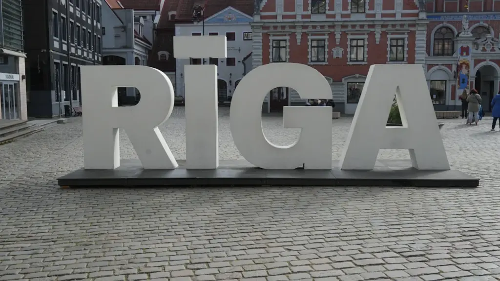 Liels, balts uzraksts RĪGA uz bruģētas ielas vēsturiskā pilsētas centrā.