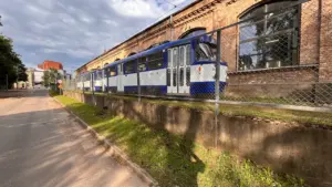 Zils un balts tramvajs brauc garām ķieģeļu ēkai Daugavpilī, pilsētas transporta infrastruktūra.