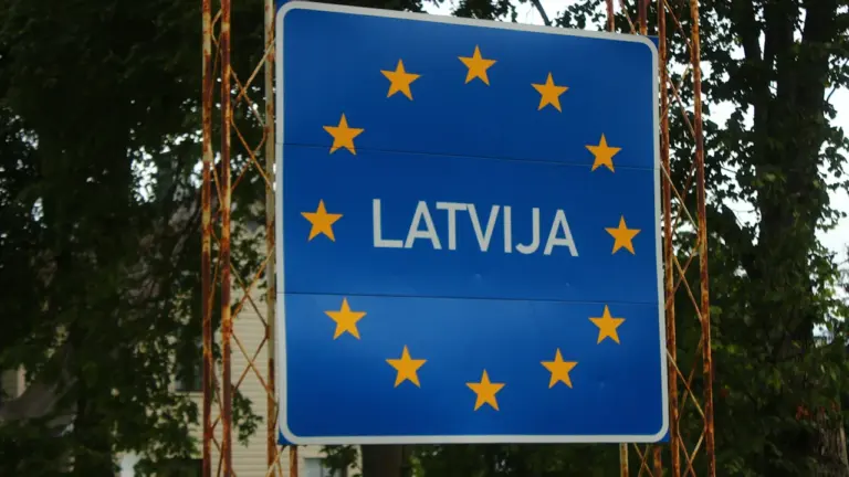 Zila zīme ar uzrakstu Latvija un Eiropas Savienības zvaigznēm uz valsts robežas fona.