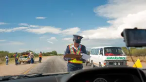 Valsts policijas darbinieks uz ceļa veic automašīnu satiksmes drošības pārbaudi dienā.