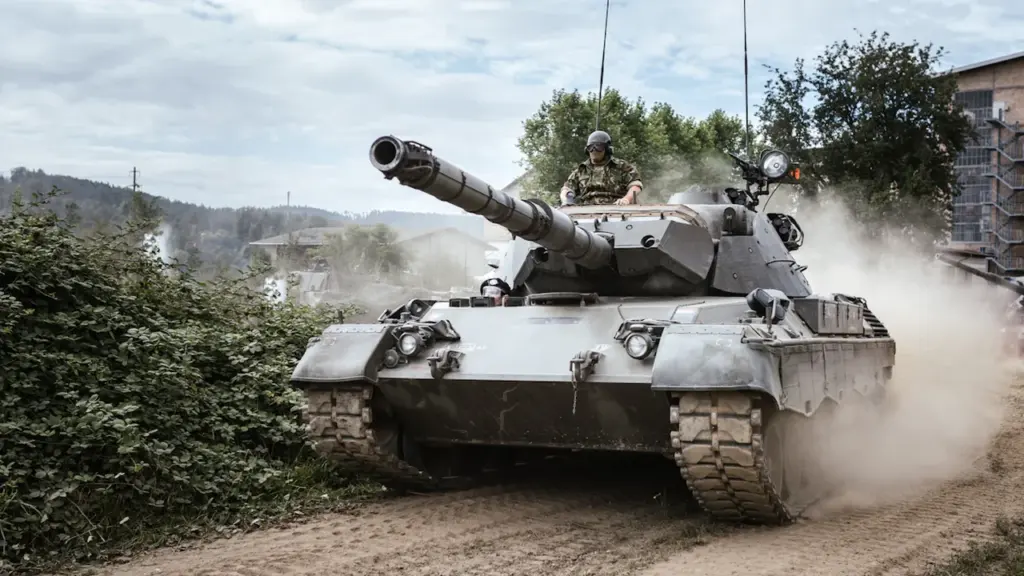 Militārais tanks pārvietojas pa zemes ceļu Austrumu pierobežas aizsardzības izbūves darbu kontekstā.