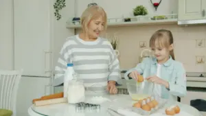 Mazmeita kopā ar vecmāmiņu virtuvē gatavo mīklu, kopīgi pavadot siltu ģimenes laiku.