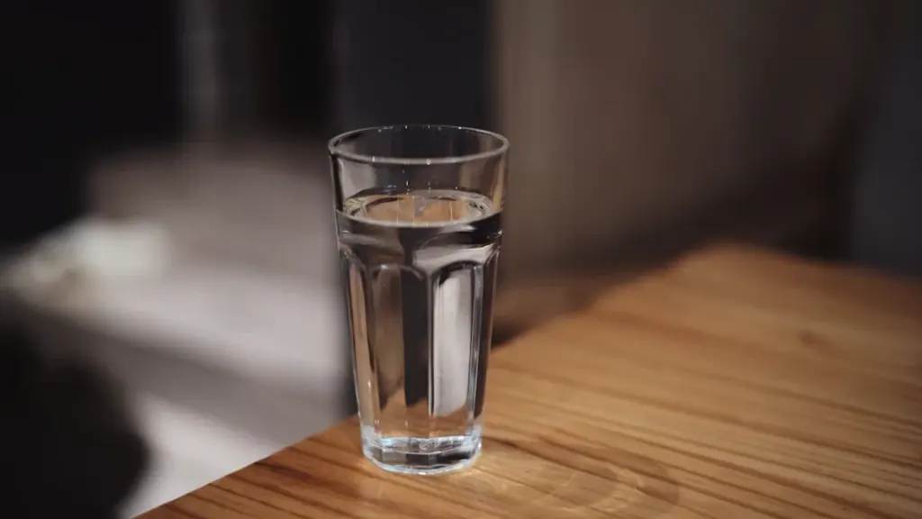Caurspīdīga ūdens glāze uz koka darba galda biroja vidē dzeršanas ieradumu veicināšanai.