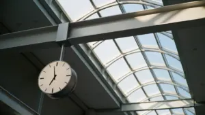 Moderns pulkstenis piestiprināts pie griestiem sabiedriskā vietā ar stiklotu jumtu.